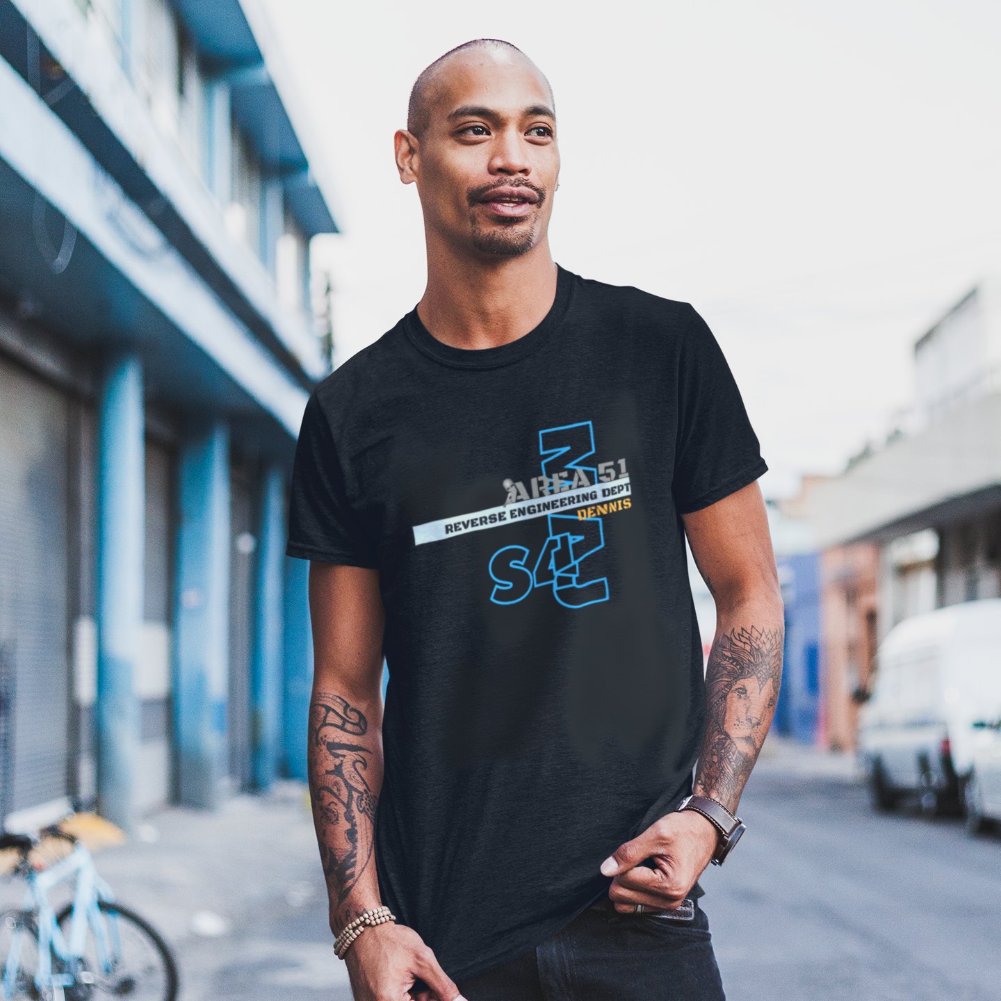 Area 51 Reverse Engineering Dept T-shirt in Black, front print, worn by a model (city street, day). AI-edited photo: the real print artwork was digitally placed on a model photo.