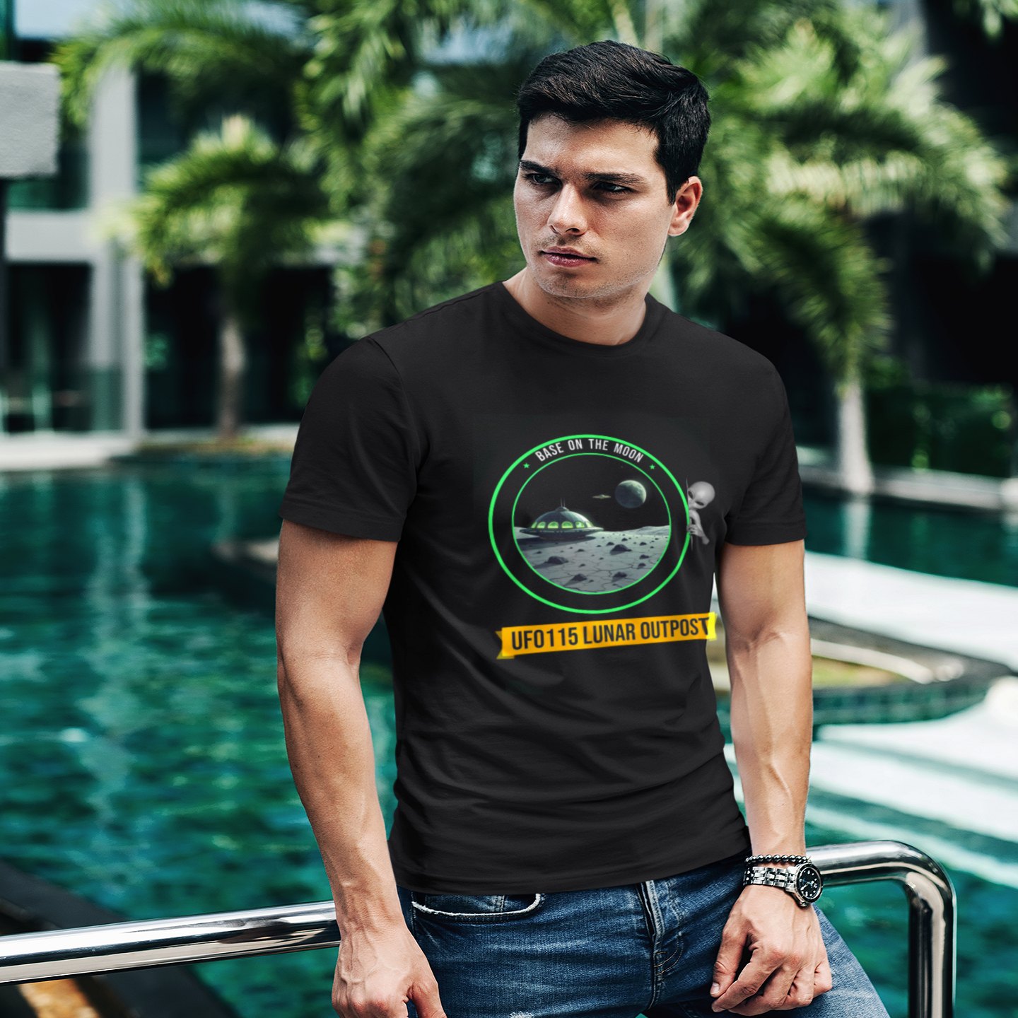 Base on the Moon Mission Patch T-shirt in Black, front print, worn by a model (tropical pool, day). AI-edited photo: the real print artwork was digitally placed on a model photo.