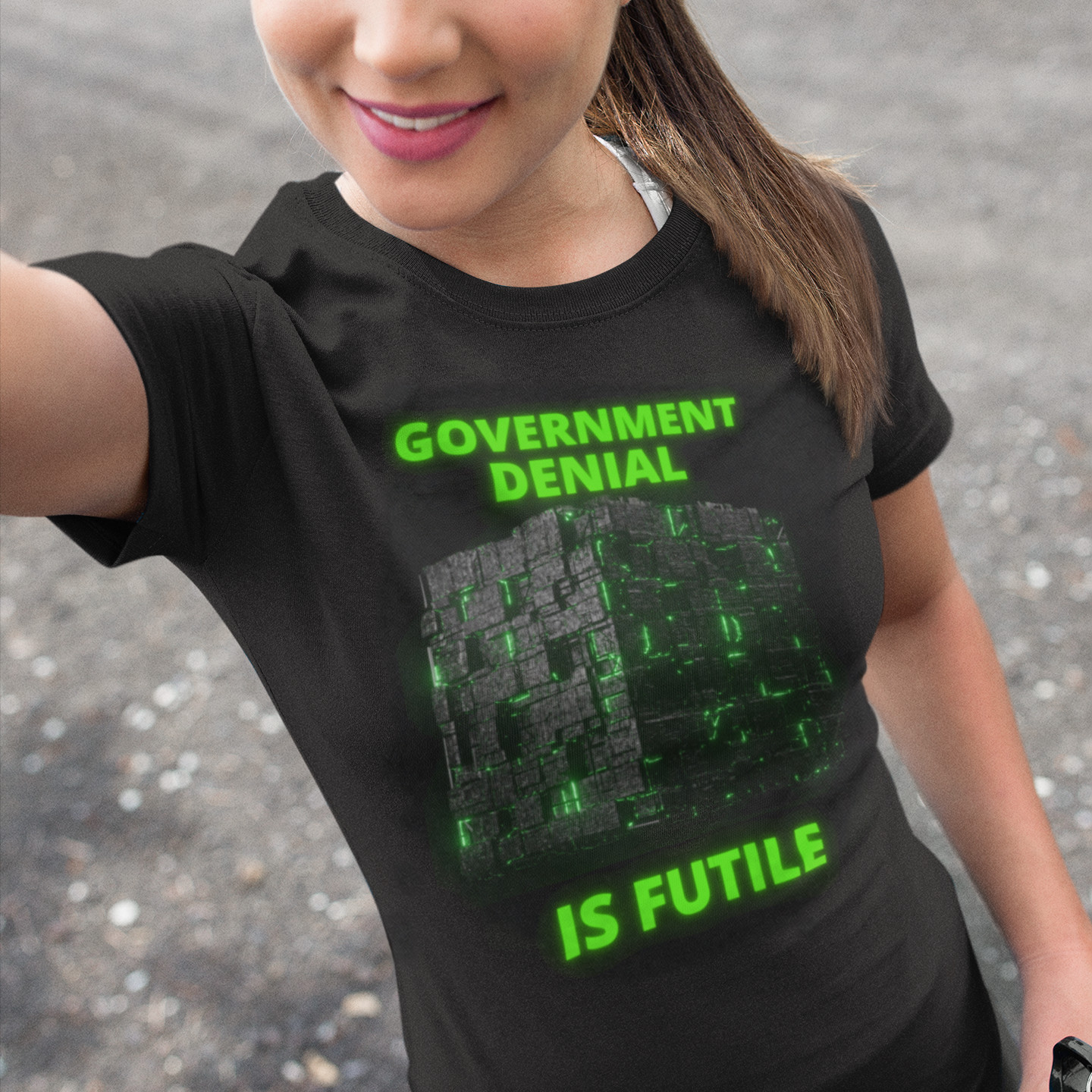 Government Denial Is Futile T-shirt in Black, front print, worn by a model (outdoor selfie, day). AI-edited photo: the real print artwork was digitally placed on a model photo.