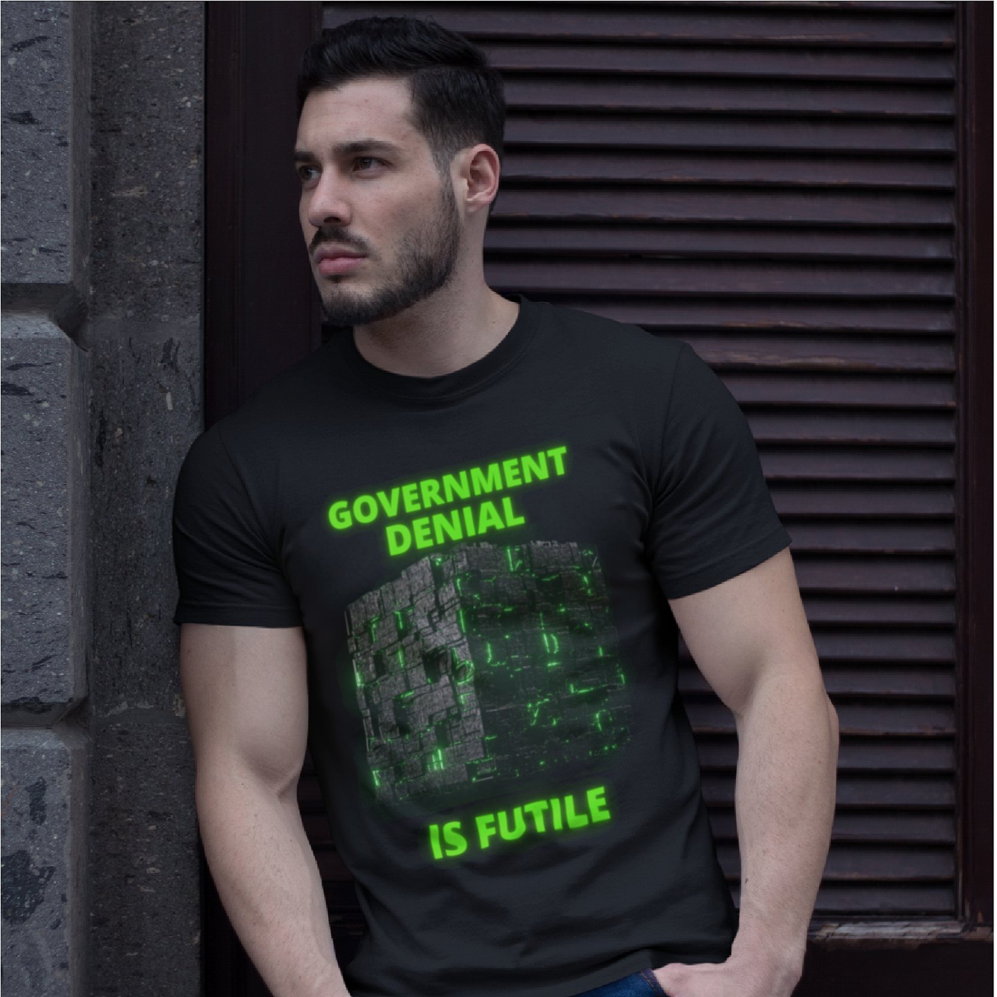 Government Denial Is Futile T-shirt in Black, front print, worn by a model (stone doorway, day). AI-edited photo: the real print artwork was digitally placed on a model photo.
