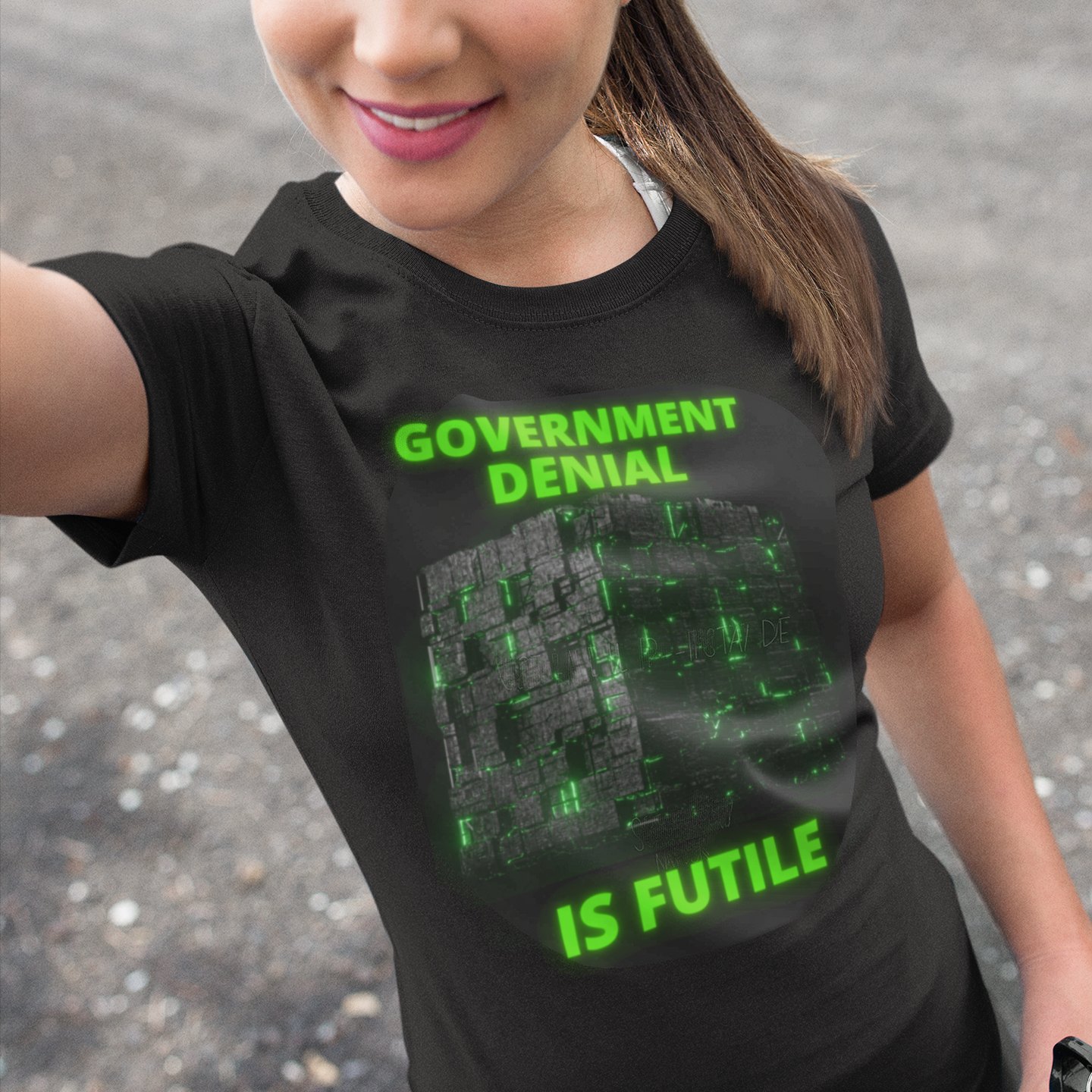 Government Denial Is Futile T-shirt in Black, front print, worn by a model (outdoor selfie, day). AI-edited photo: the real print artwork was digitally placed on a model photo.
