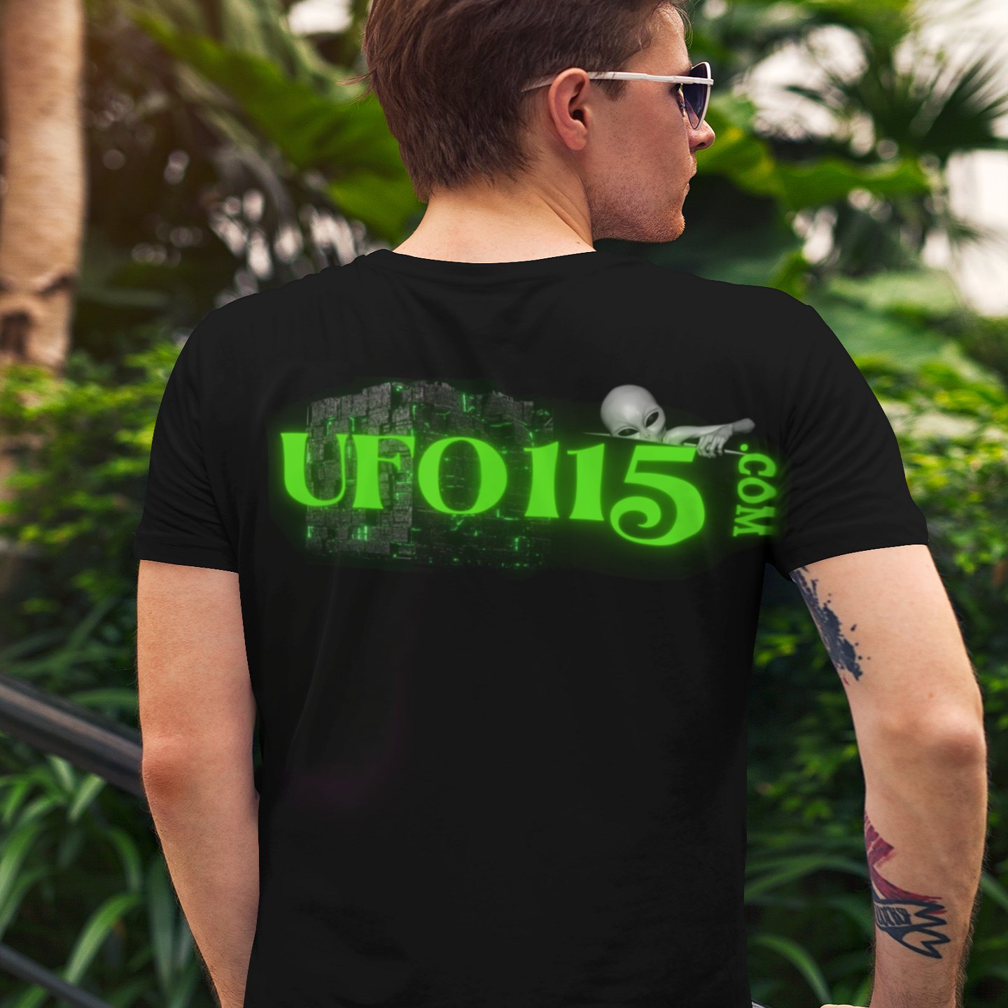 Government Denial Is Futile T-shirt in Black, back print, worn by a model (tropical garden, day (back)). AI-edited photo: the real print artwork was digitally placed on a model photo.