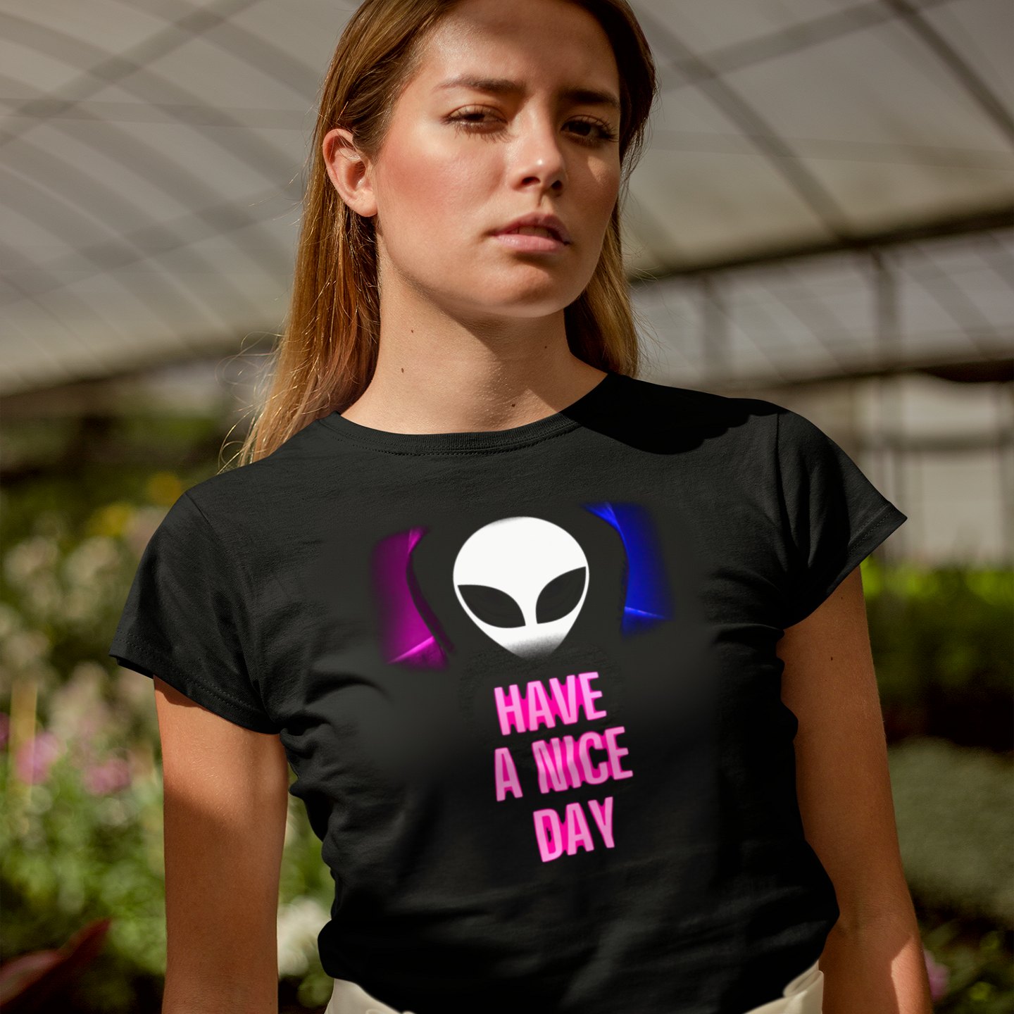 Have a Nice Day Alien T-shirt in Black, front print, worn by a model (greenhouse, day). AI-edited photo: the real print artwork was digitally placed on a model photo.