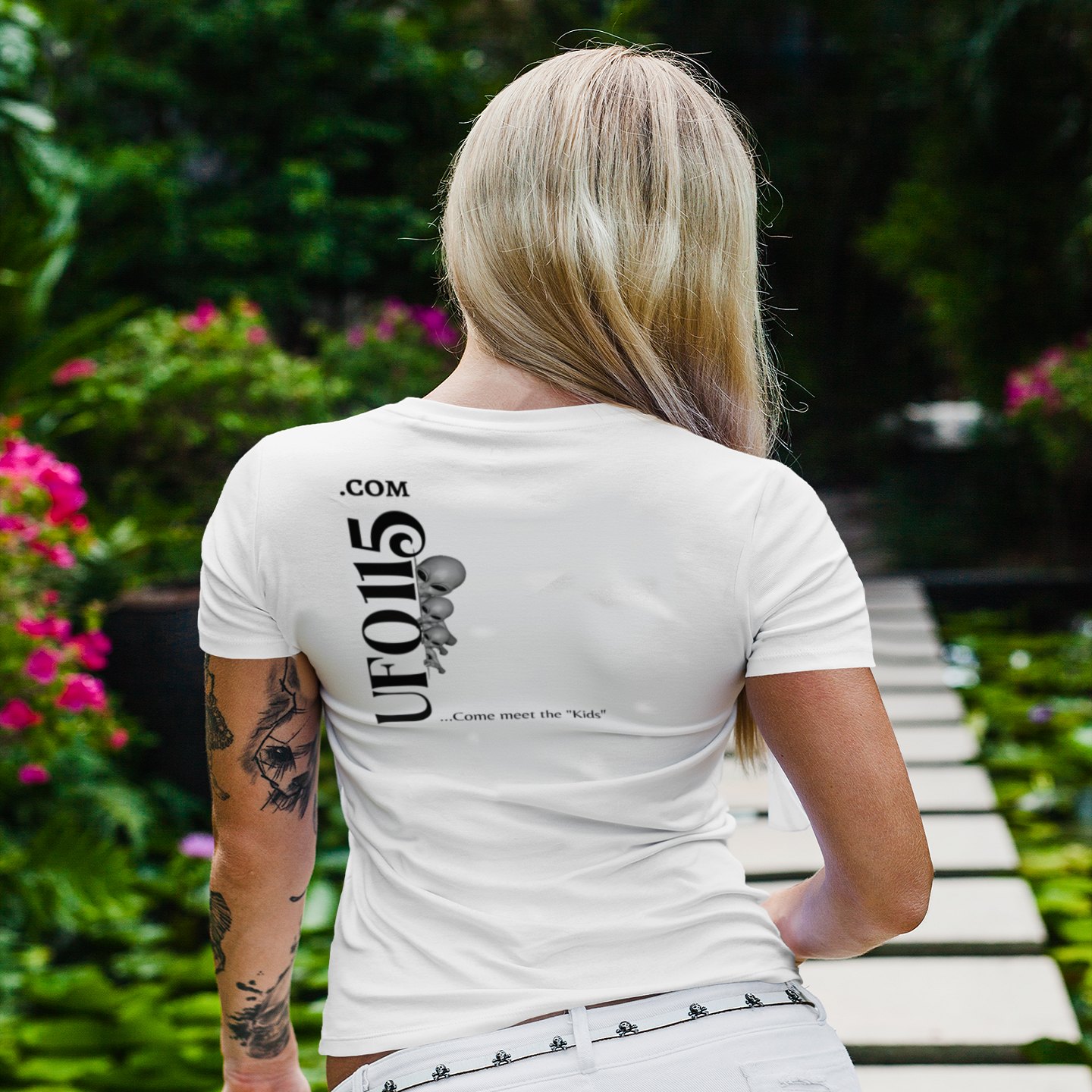 No More Secrets Alien Face T-shirt in White, back print, worn by a model (tropical garden walkway (back)). AI-edited photo: the real print artwork was digitally placed on a model photo.