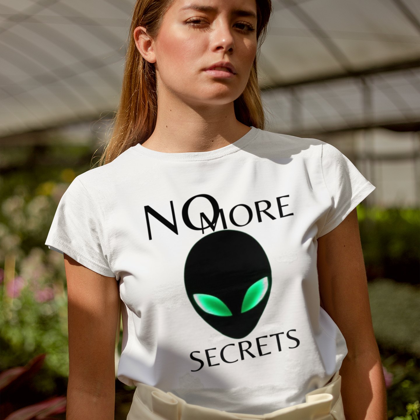No More Secrets Alien Face T-shirt in White, front print, worn by a model (greenhouse, day). AI-edited photo: the real print artwork was digitally placed on a model photo.