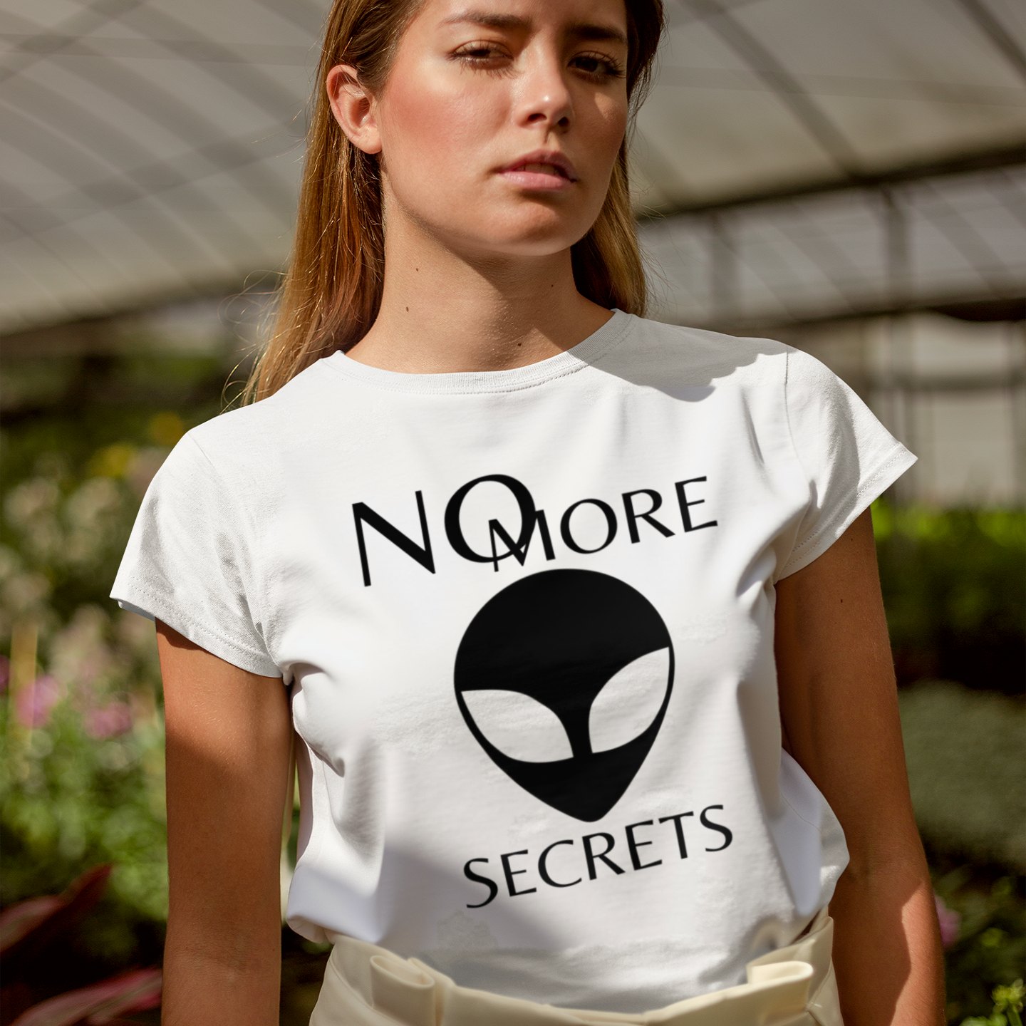 No More Secrets Black Alien Face T-shirt in White, front print, worn by a model (greenhouse, day). AI-edited photo: the real print artwork was digitally placed on a model photo.