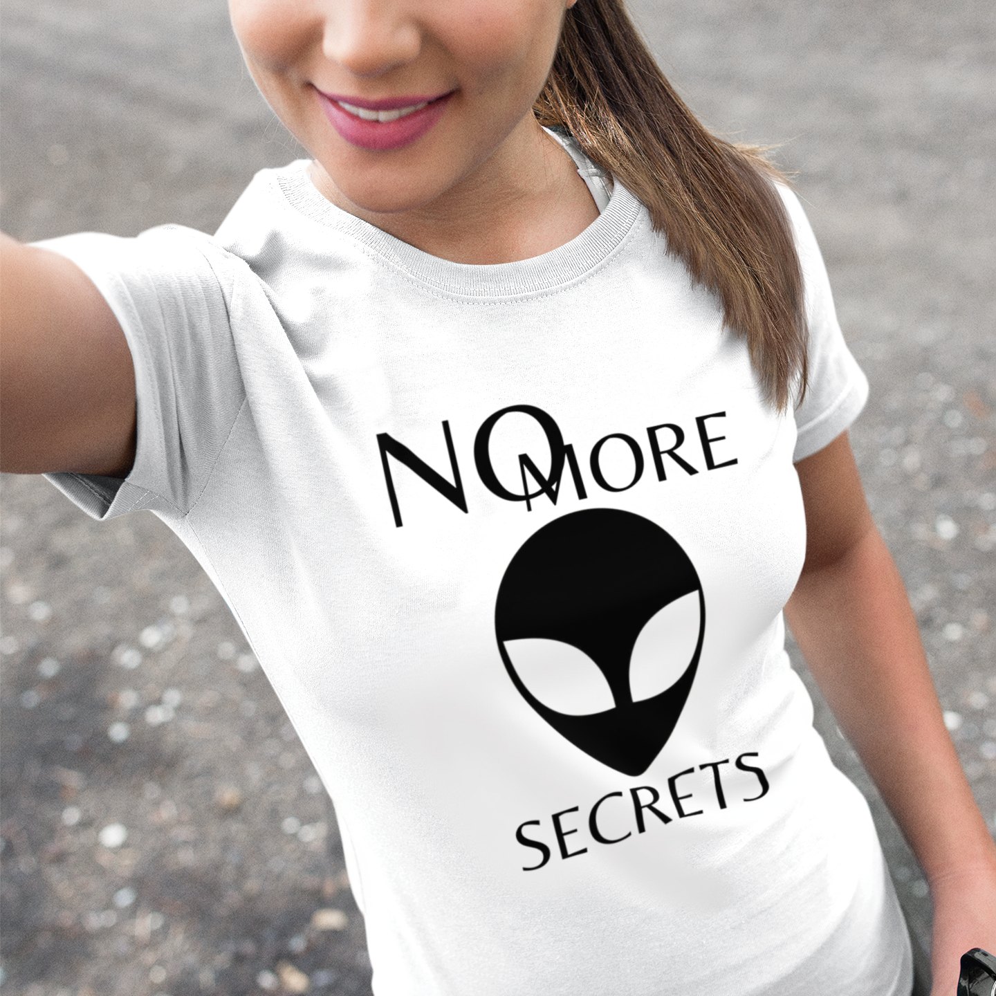 No More Secrets Black Alien Face T-shirt in White, front print, worn by a model (outdoor selfie, day). AI-edited photo: the real print artwork was digitally placed on a model photo.