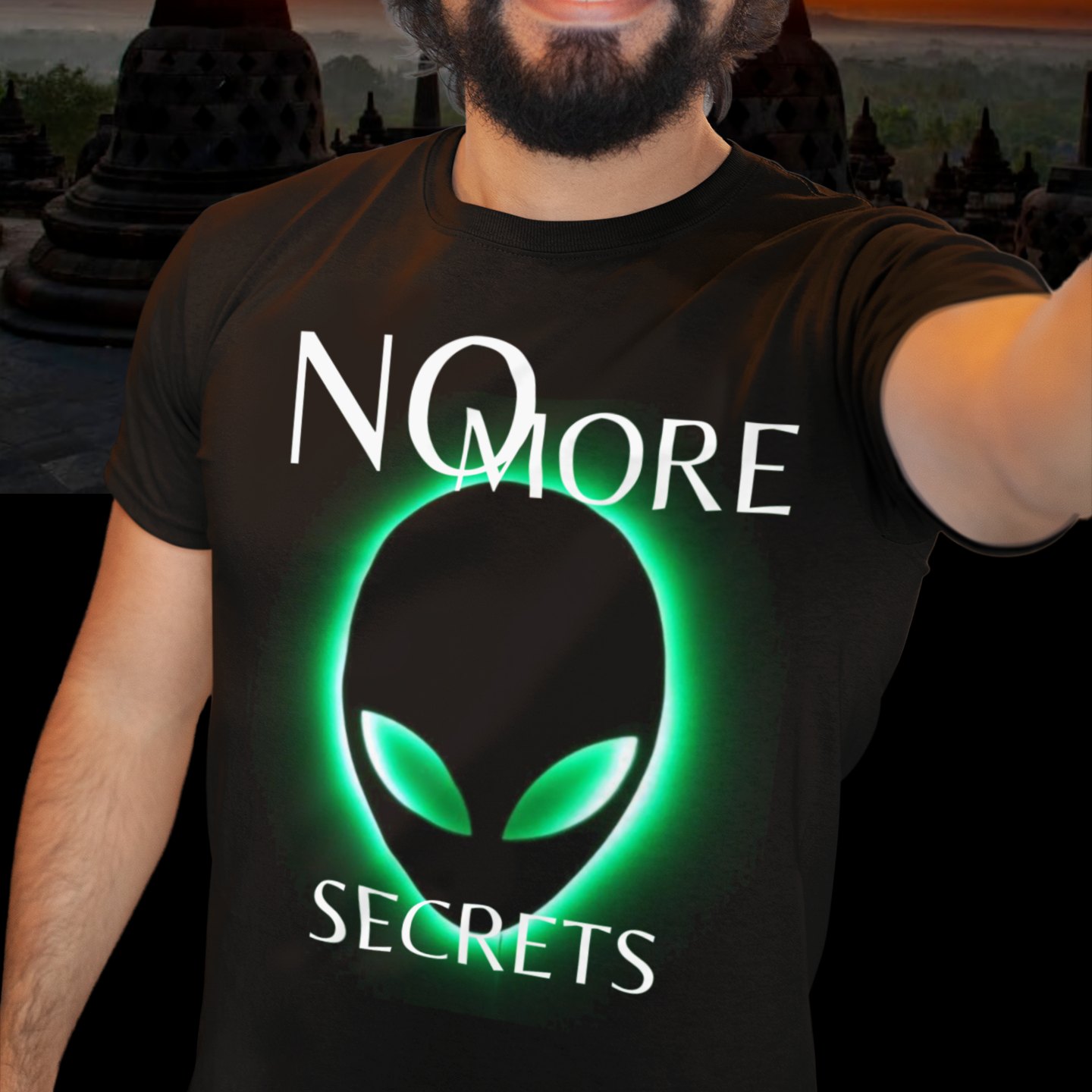 No More Secrets Green Glow Alien Face T-shirt in Black, front print, worn by a model (temple at sunset). AI-edited photo: the real print artwork was digitally placed on a model photo.