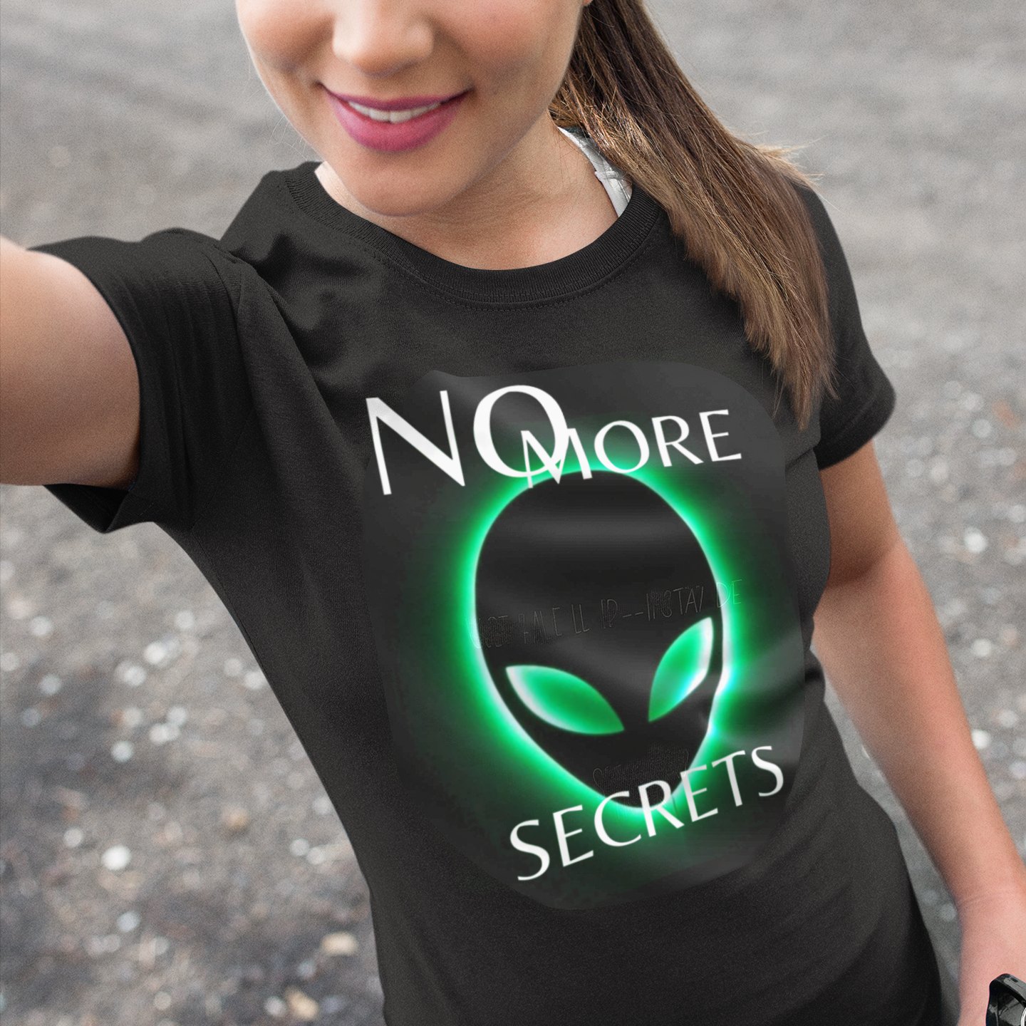 No More Secrets Green Glow Alien Face T-shirt in Black, front print, worn by a model (outdoor selfie, day). AI-edited photo: the real print artwork was digitally placed on a model photo.