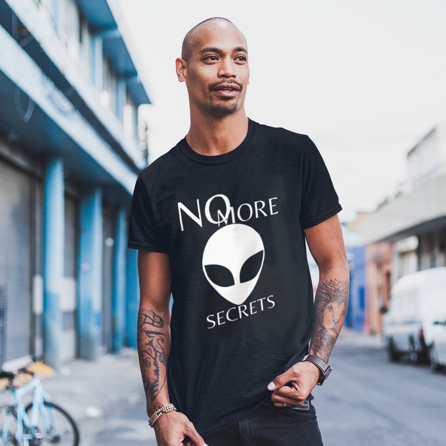 No More Secrets Pine Gap T-shirt in Black, front print, worn by a model (city street, day). AI-edited photo: the real print artwork was digitally placed on a model photo.