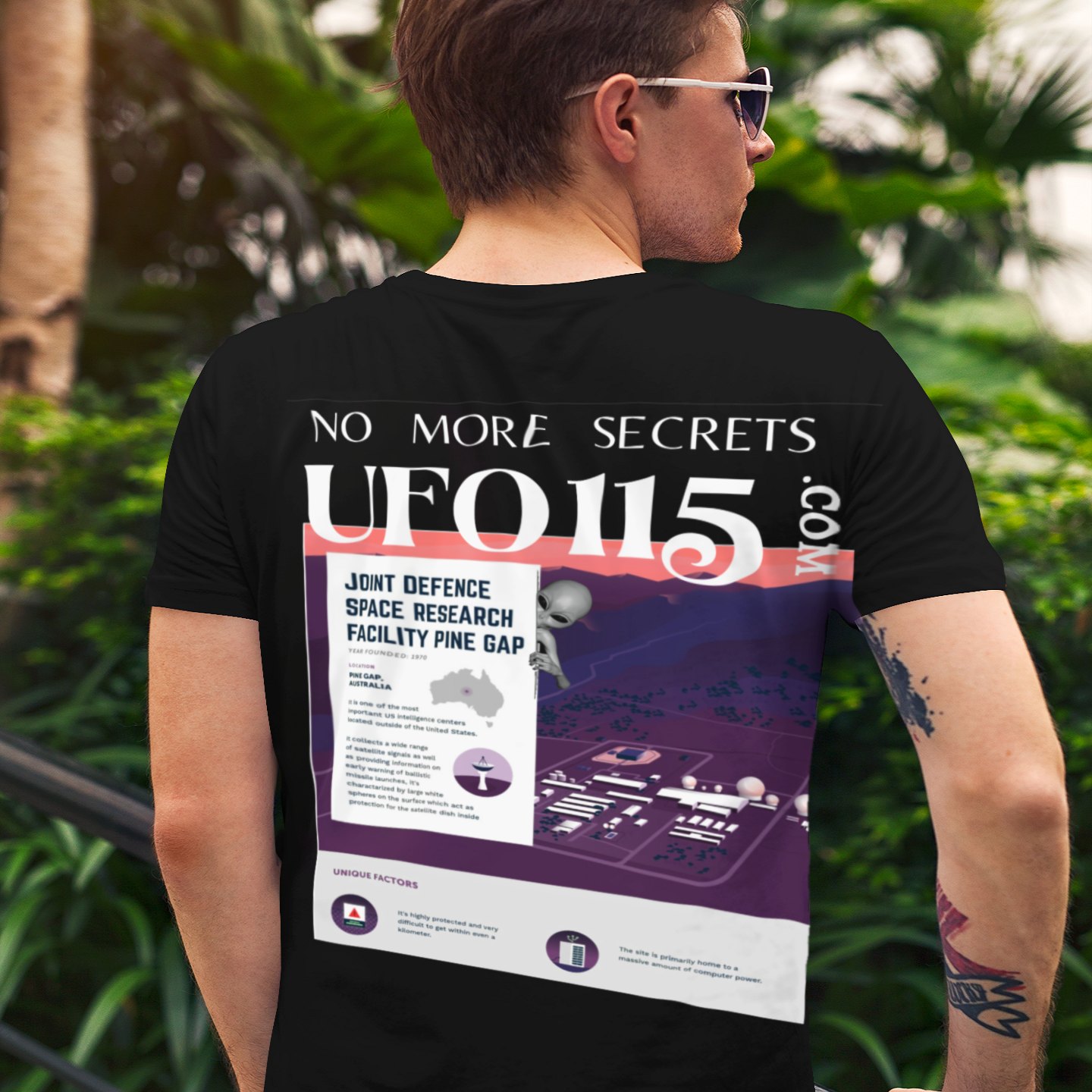 No More Secrets Pine Gap T-shirt in Black, back print, worn by a model (tropical garden, day (back)). AI-edited photo: the real print artwork was digitally placed on a model photo.