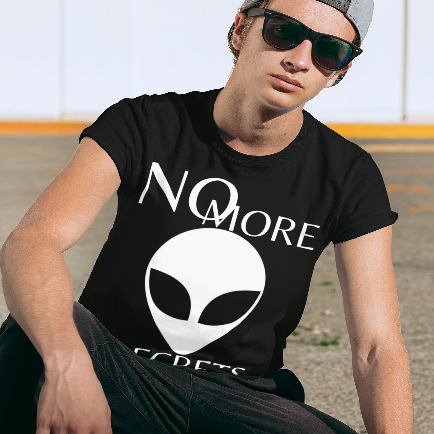 No More Secrets Porton Down T-shirt in Black, front print, worn by a model (urban crouch, day). AI-edited photo: the real print artwork was digitally placed on a model photo.