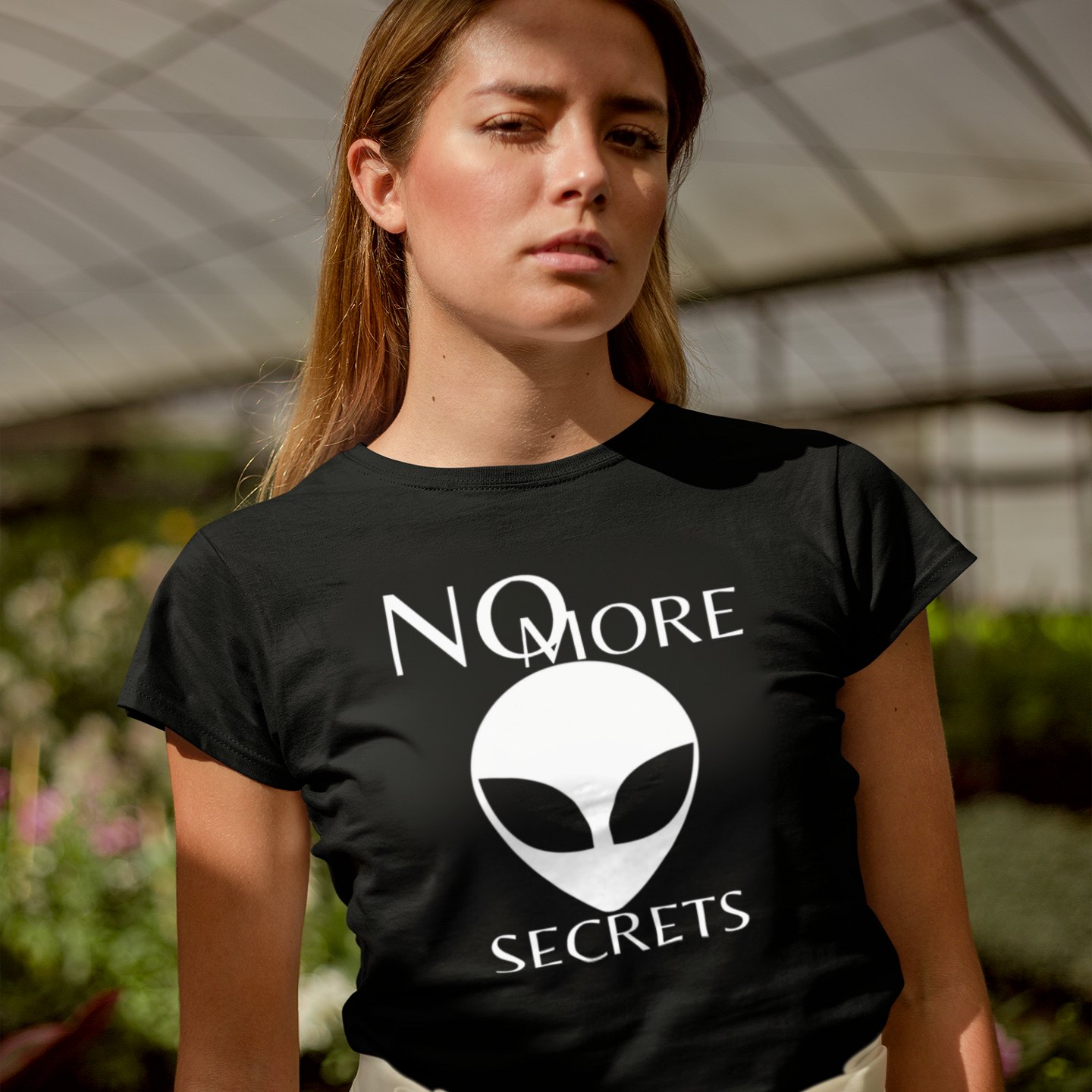 No More Secrets South China Sea T-shirt in Black, front print, worn by a model (greenhouse, day). AI-edited photo: the real print artwork was digitally placed on a model photo.