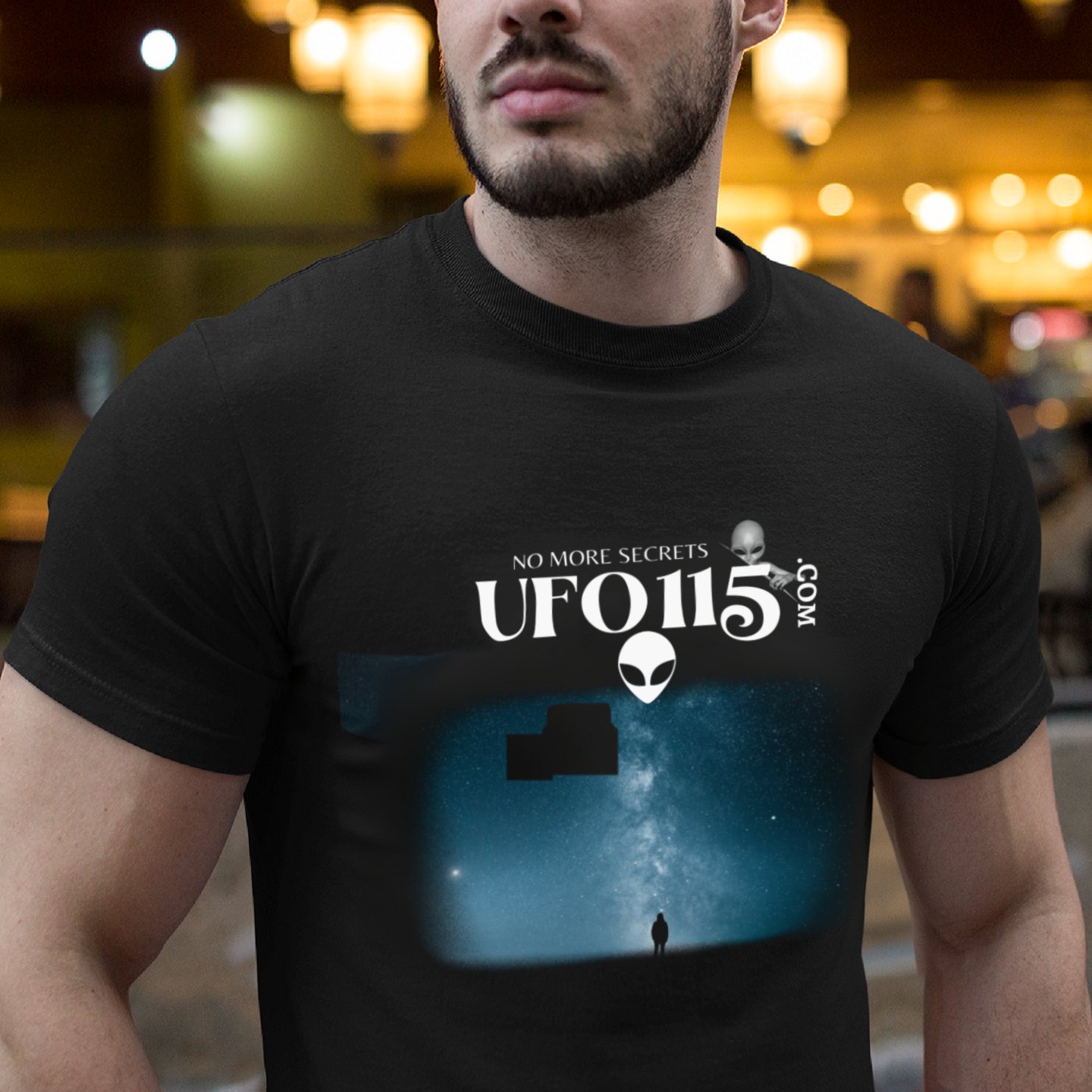 Sky Watcher Blue Solitude T-shirt in Black, front print, worn by a model (bar lights, evening). AI-edited photo: the real print artwork was digitally placed on a model photo.