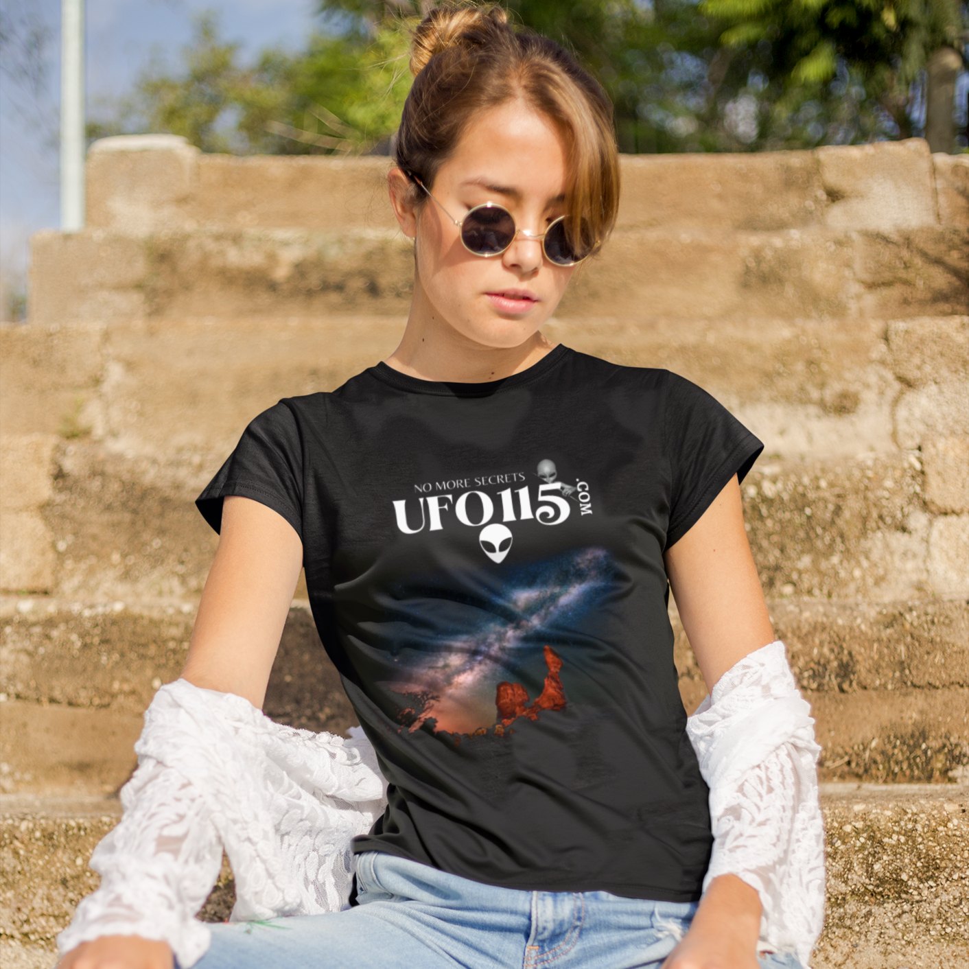 Sky Watcher Milky Way Canyon T-shirt in Black, front print, worn by a model (stone steps, daylight travel). AI-edited photo: the real print artwork was digitally placed on a model photo.