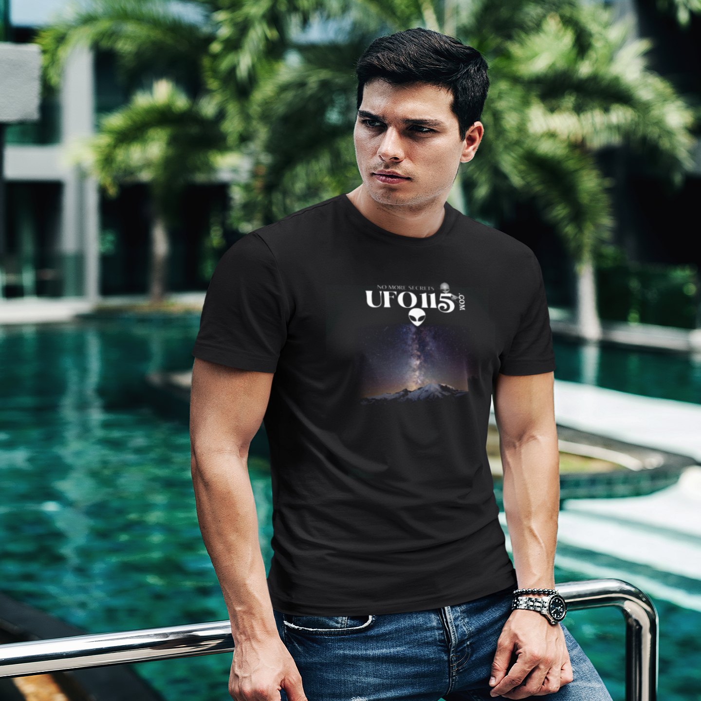Sky Watcher Mountain Light T-shirt in Black, front print, worn by a model (tropical pool, day). AI-edited photo: the real print artwork was digitally placed on a model photo.